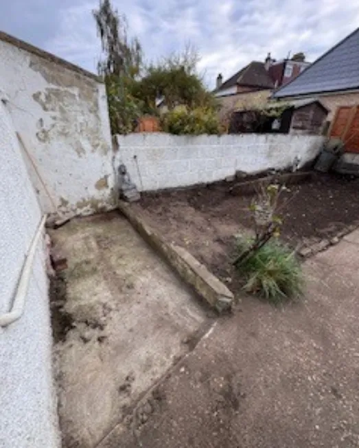 Garden corner cleared back to bare soil beside the wall